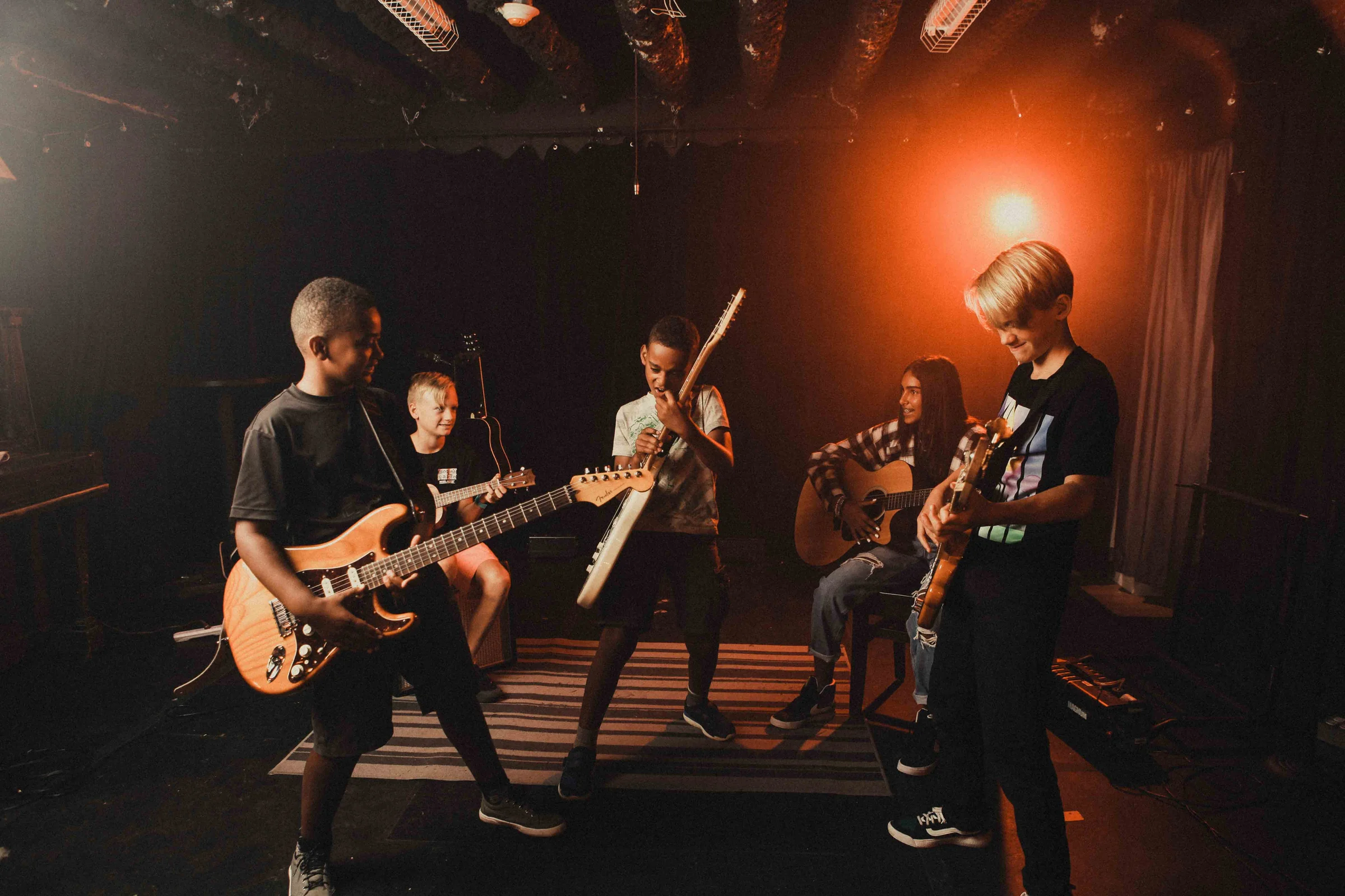 Kids playing guitars on a stage with a orange light in the background