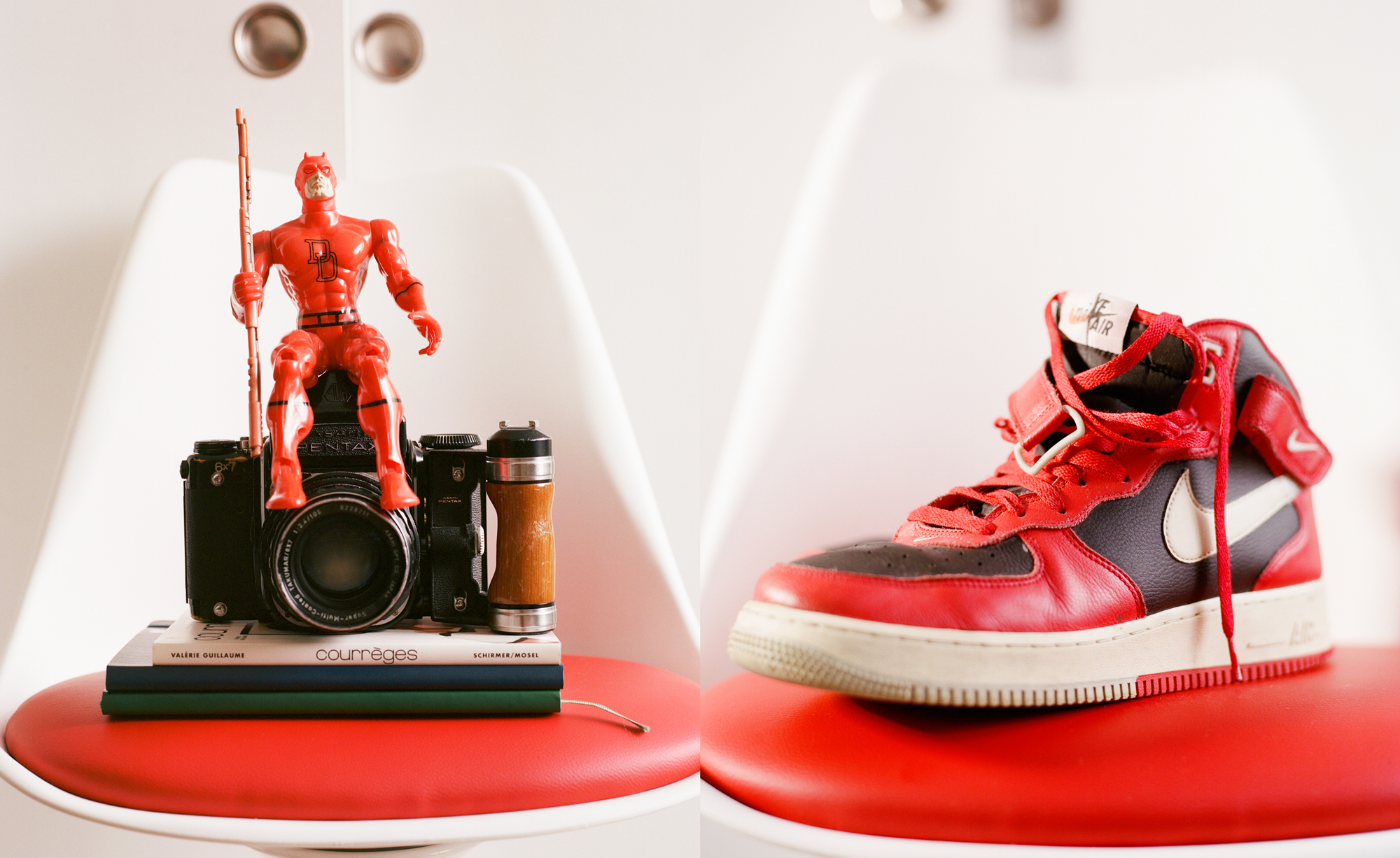 Red Daredevil figure sits on a vintage camera on books; red and black Nike sneaker on red chair.
