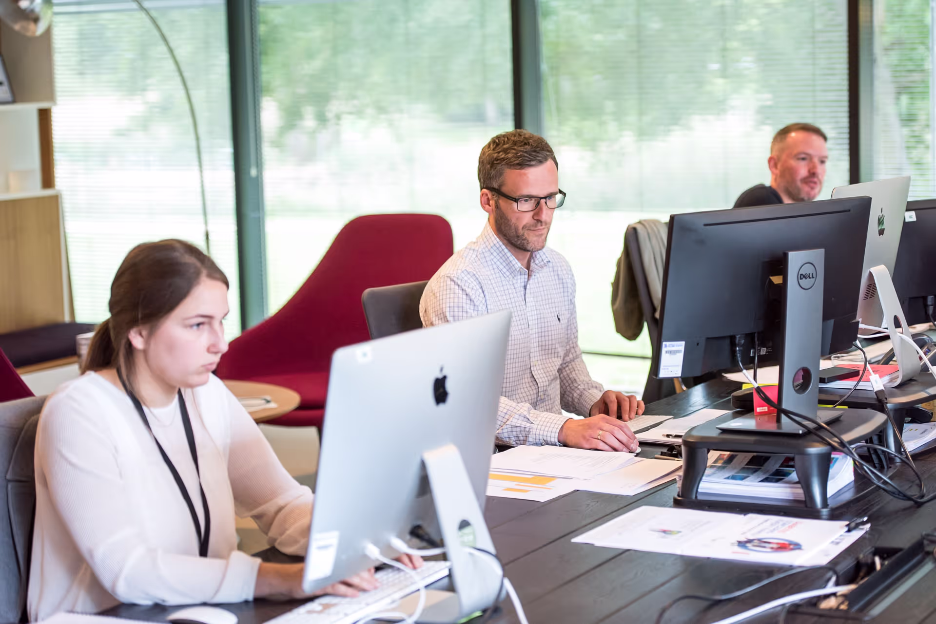 A photo of two men and a woman in an office working at their desktop computers. 