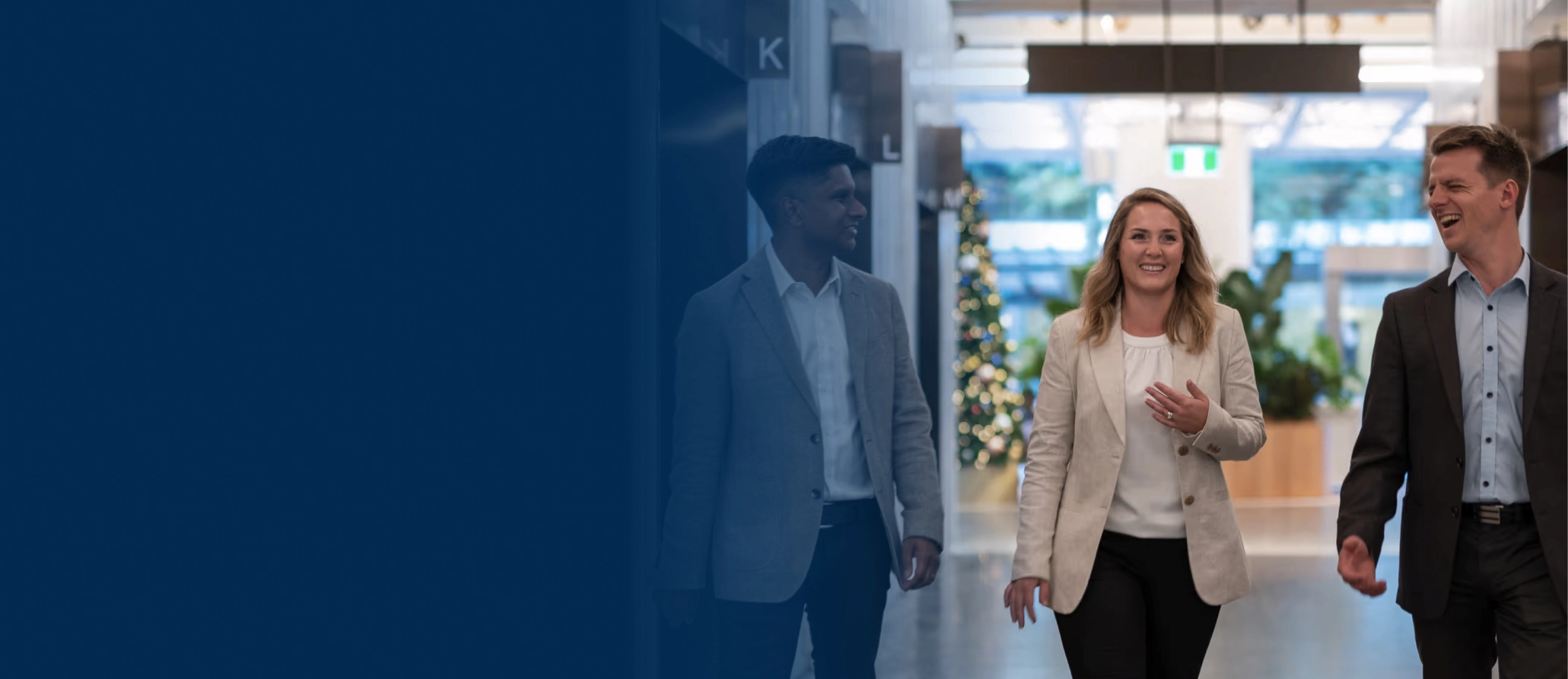 Three professionals, two men and one woman, walking and chatting in a modern office corridor.