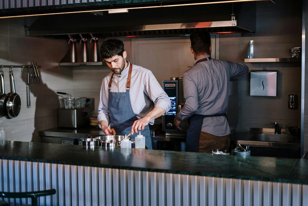 Two chefs in a restaurant kitchen preparing food wearing aprons.