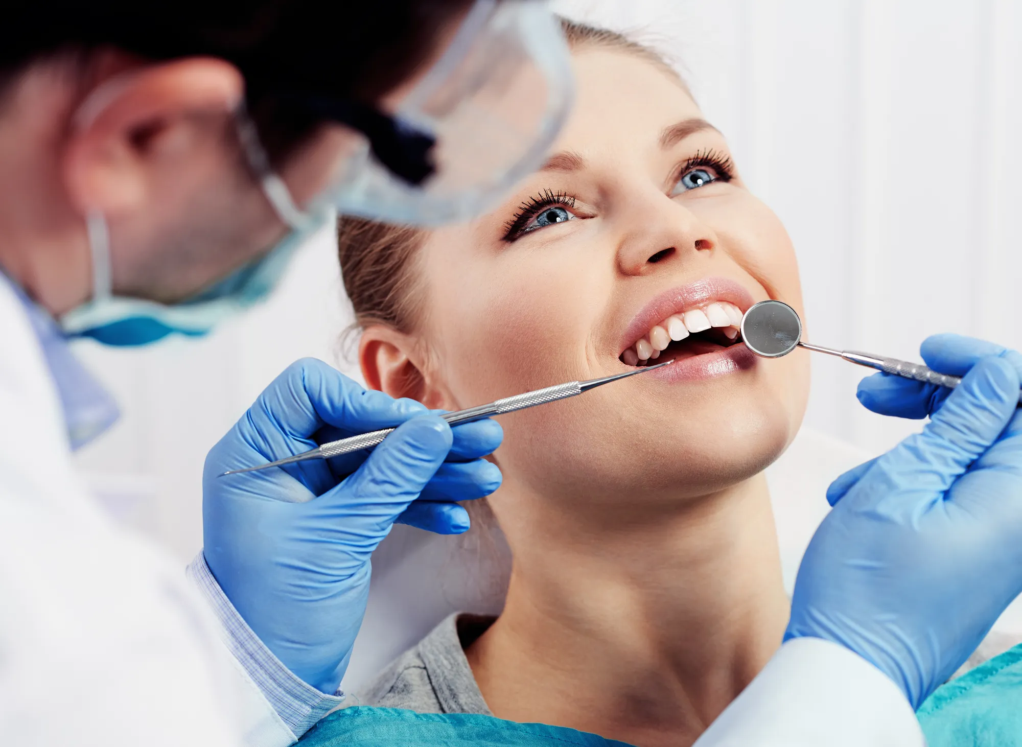 Dentist examining a smiling patient’s teeth with a mirror and probe.