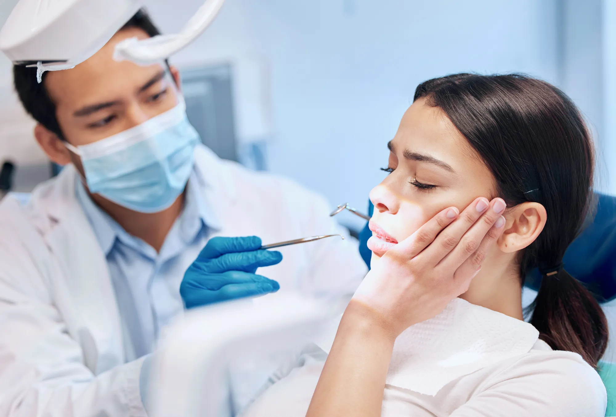 Dentist examining a woman who is holding her cheek in pain during an urgent dental visit.