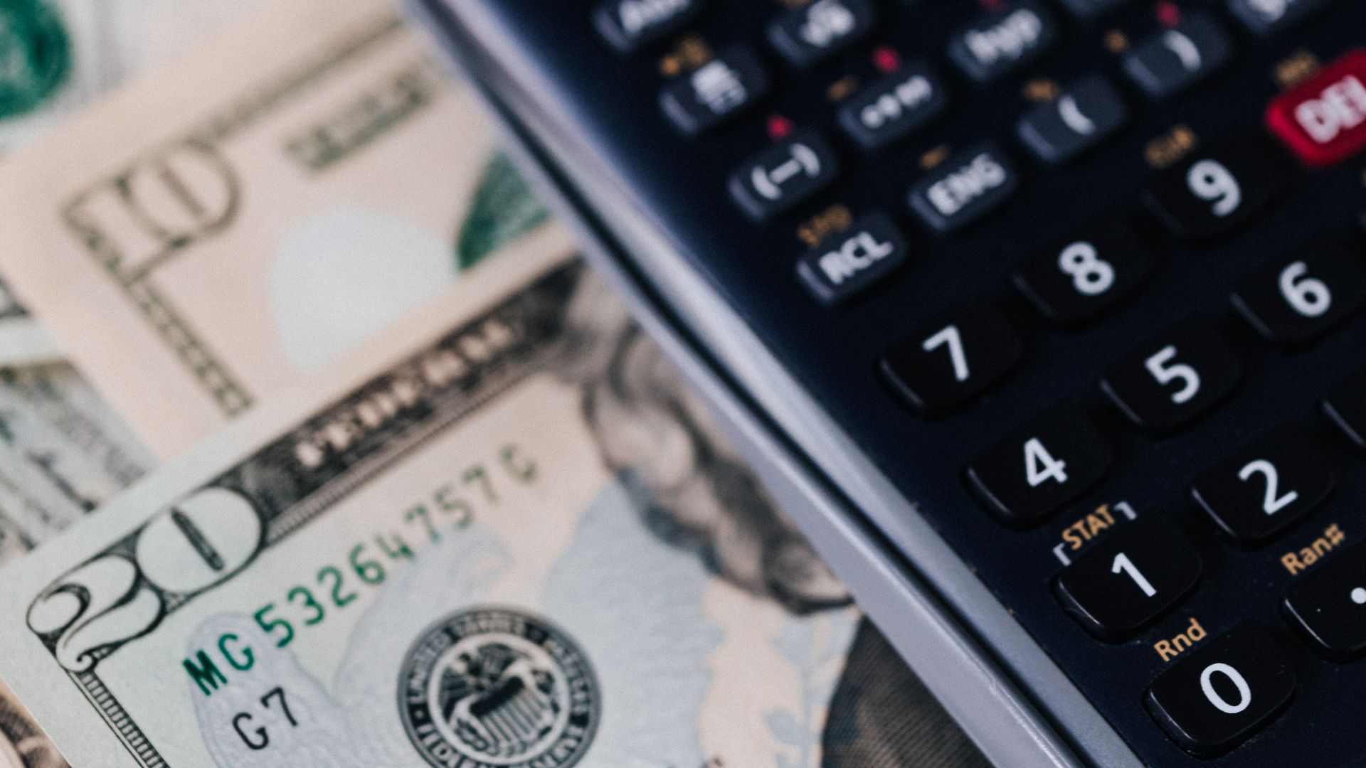 A calculator resting on a stack of banknotes, representing the hidden costs of cheap 3PL fulfillment
