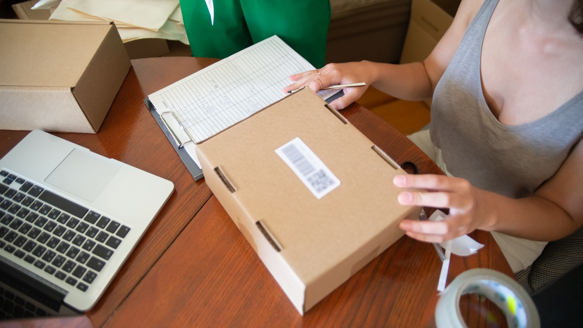 A small business owner sitting at a table packing ecommerce orders into boxes
