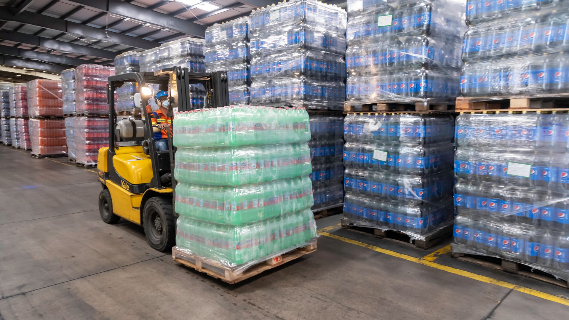 Forklift operator moving stacked pallets of oversized goods in a busy warehouse