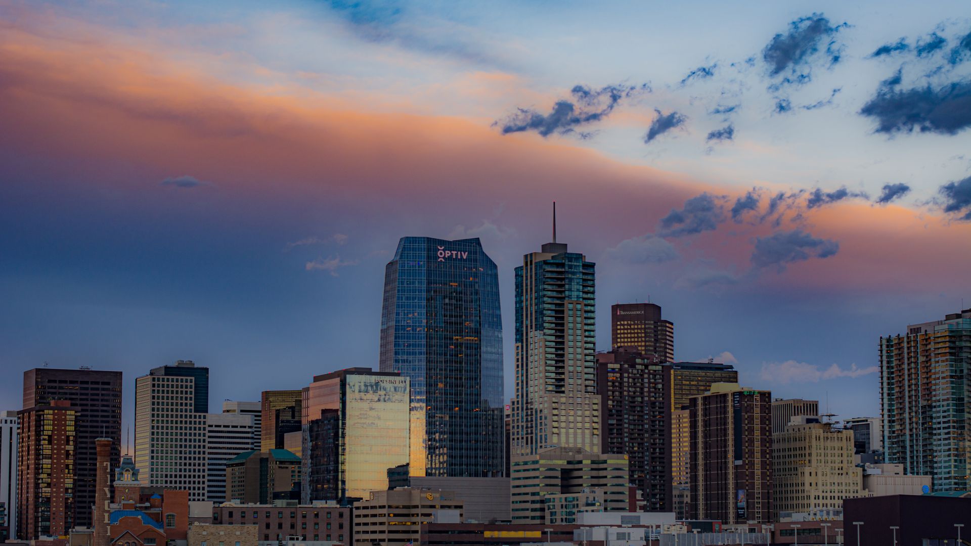 Downtown Denver skyline at sunset with the Rocky Mountains behind it