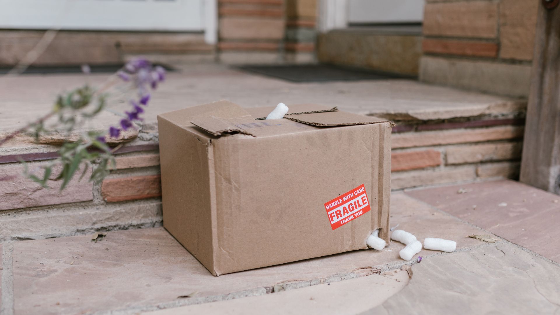 A damaged cardboard parcel marked fragile sitting on porch steps with packing peanuts spilling out