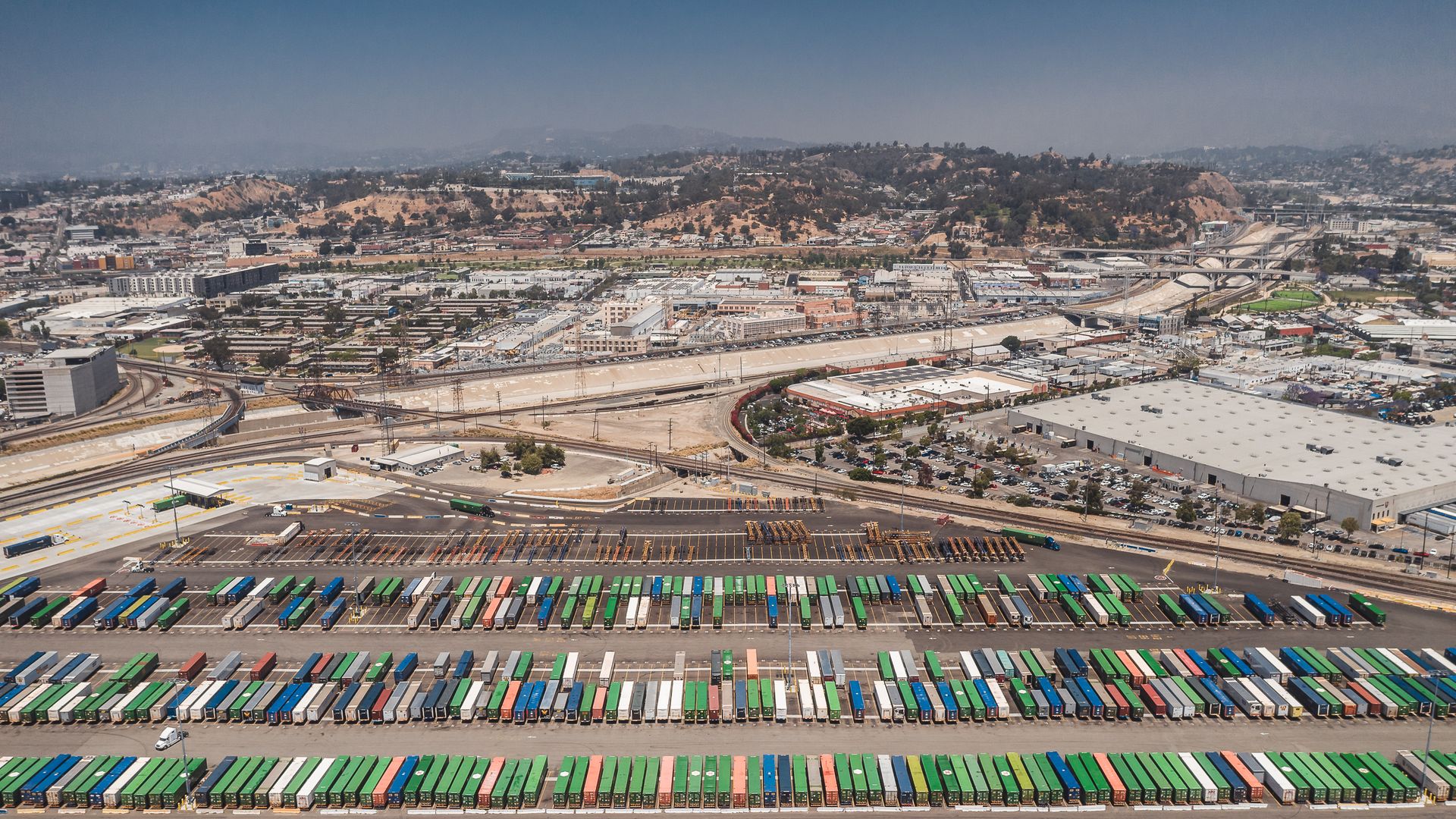 Aerial view of shipping containers stacked at a port beside a sprawling Southern California cityscape