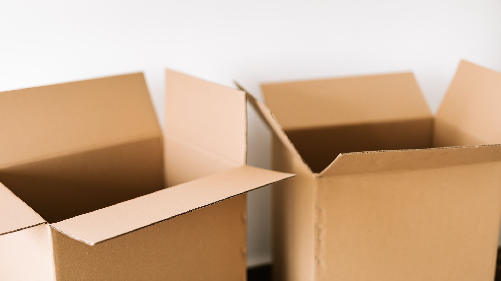 Two open empty cardboard shipping boxes against a white wall