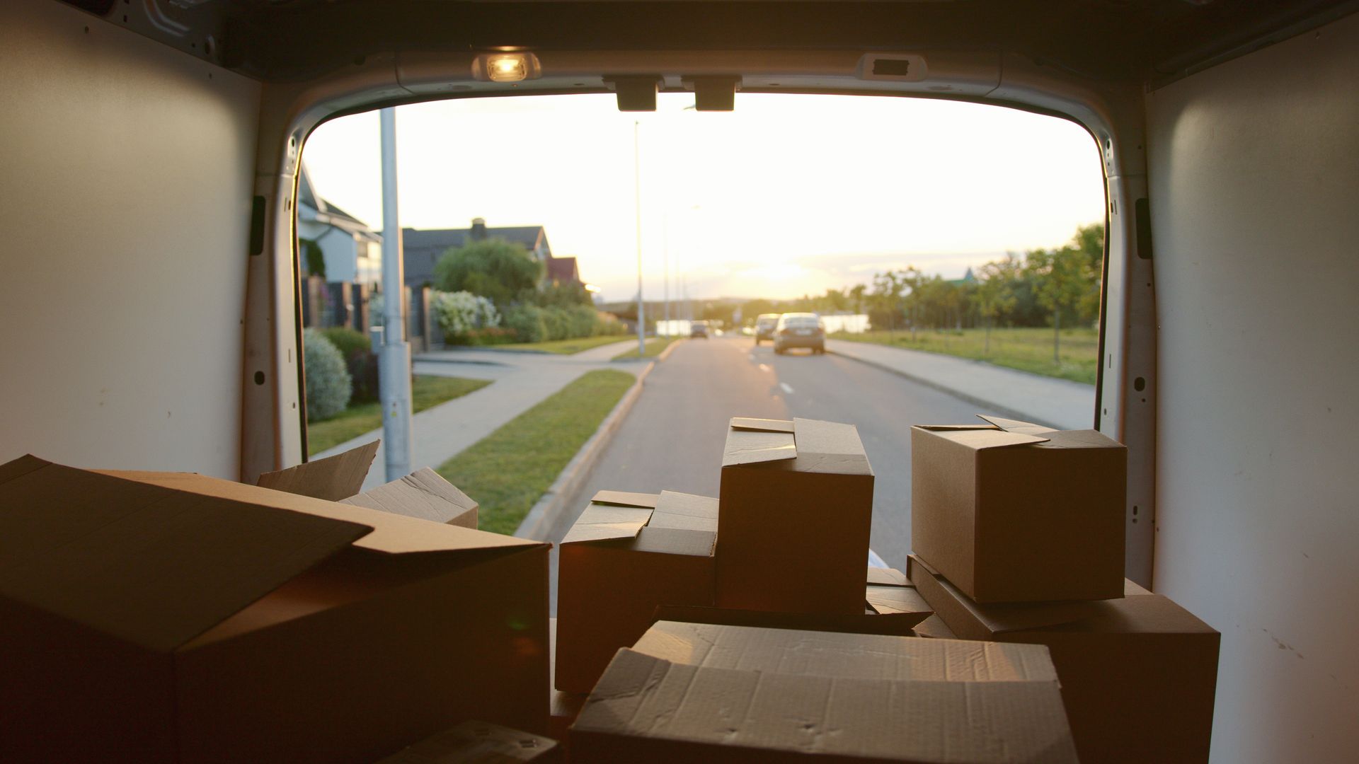 Cardboard boxes stacked in the back of a delivery van on a residential street at sunset