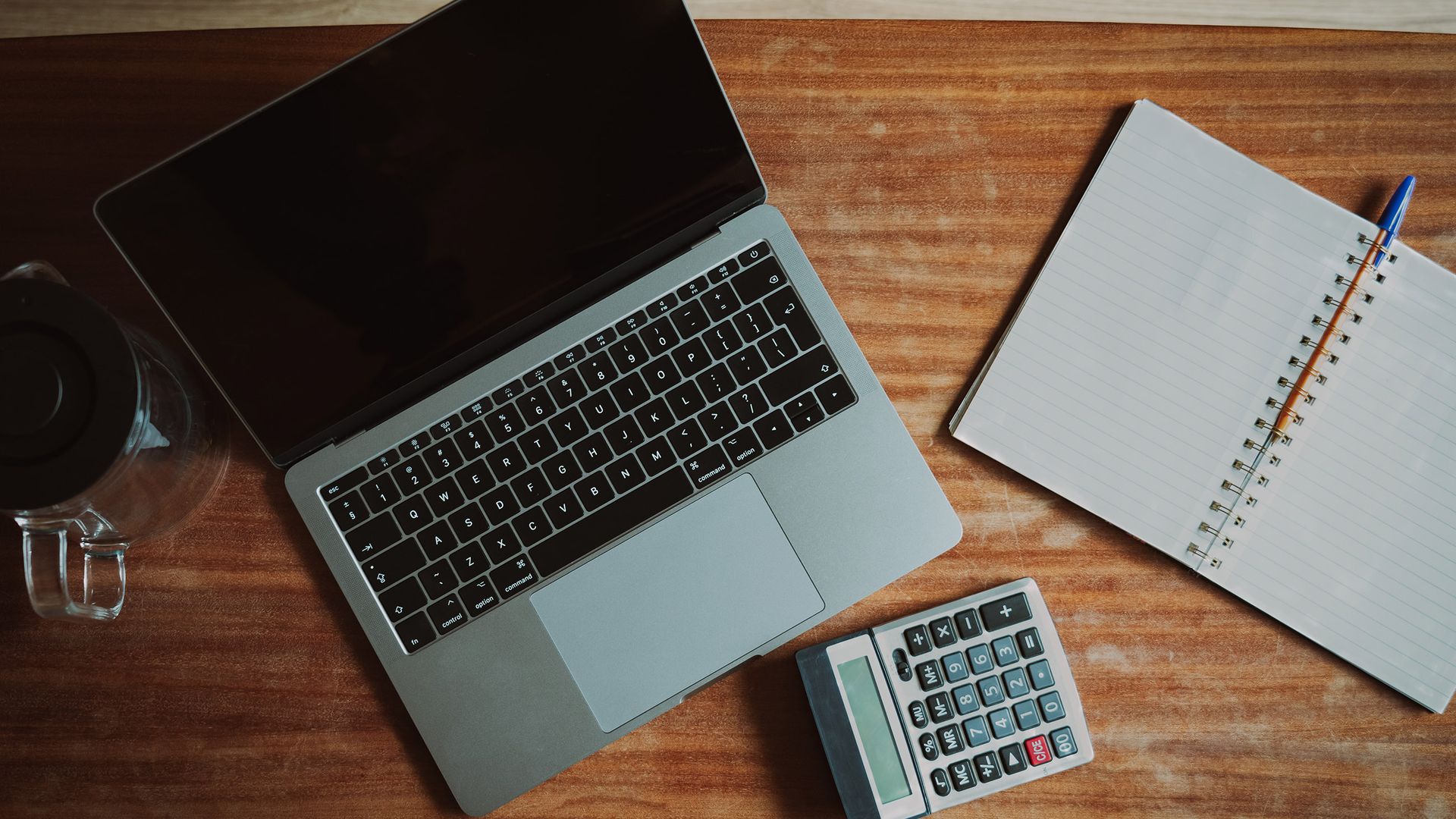 Laptop, calculator and open notebook on a wooden desk