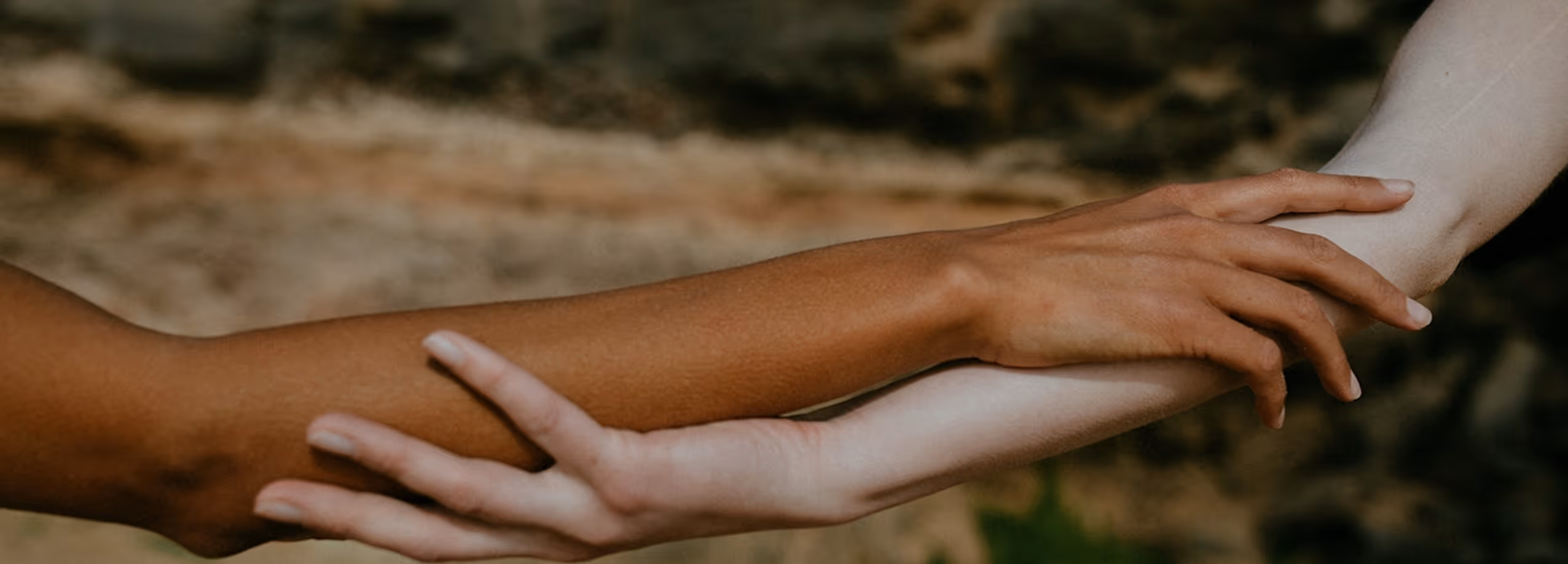 Close-up of two arms, one dark-skinned gently holding the wrist of a light-skinned arm.