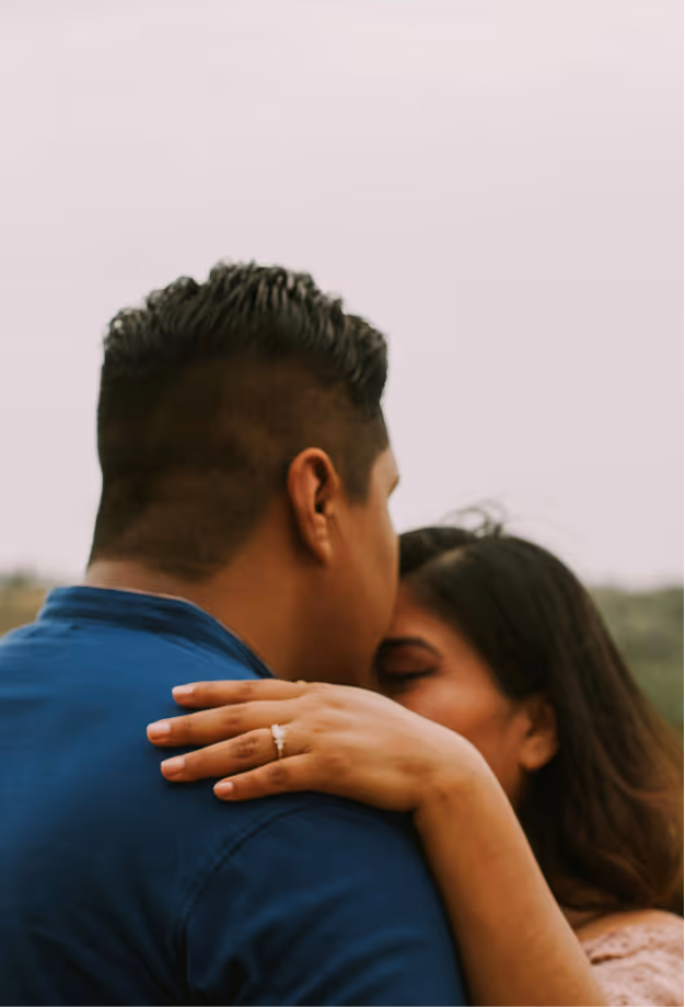Woman embracing man with her hand showing an engagement ring on his shoulder.