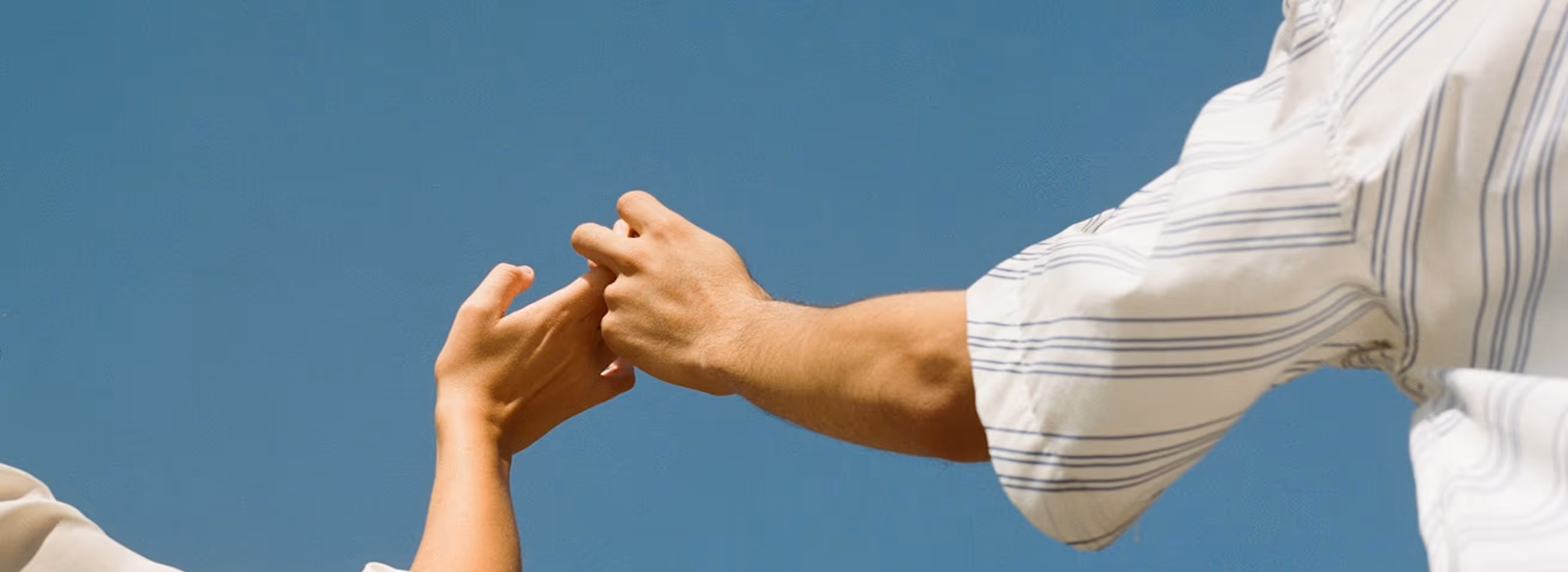 Two people linking fingers against a clear blue sky background.