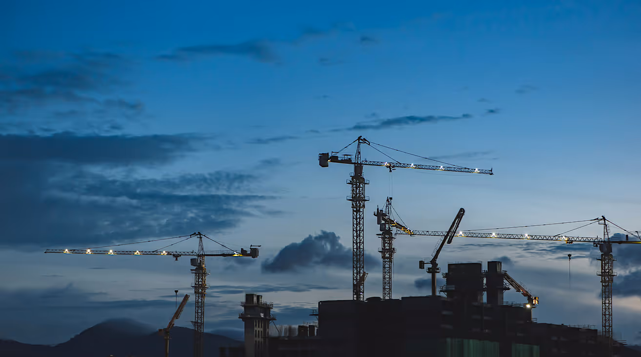 Mehrere Baukräne auf einer Baustelle, kurz nach Sonnenuntergang