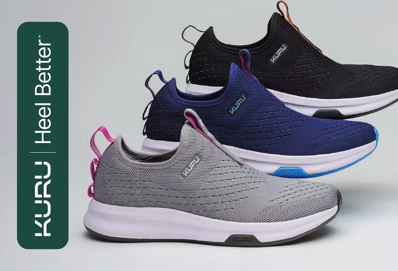 A postcard featuring three pairs of KURU slip-on athletic shoes in black, navy, and gray with pink accents, stacked diagonally against a light background. The left side displays the green KURU logo vertically alongside the slogan “Heel Better™.”
