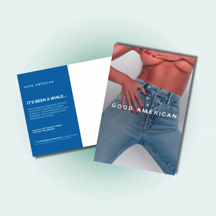 Front and back of a Good American postcard. The front features a bold photo of a woman wearing unbuttoned high-waisted blue jeans, cropped at the chest, with the Good American logo across the denim. The back has a blue and white design with the headline “IT’S BEEN A WHILE…” and copy inviting the customer to return and shop, including a 20% off discount code.
