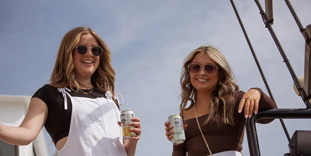 A couple of friends smile as they enjoy a Coldstream beverage on a hot, sunny day aboard the Tall Ship Silva.