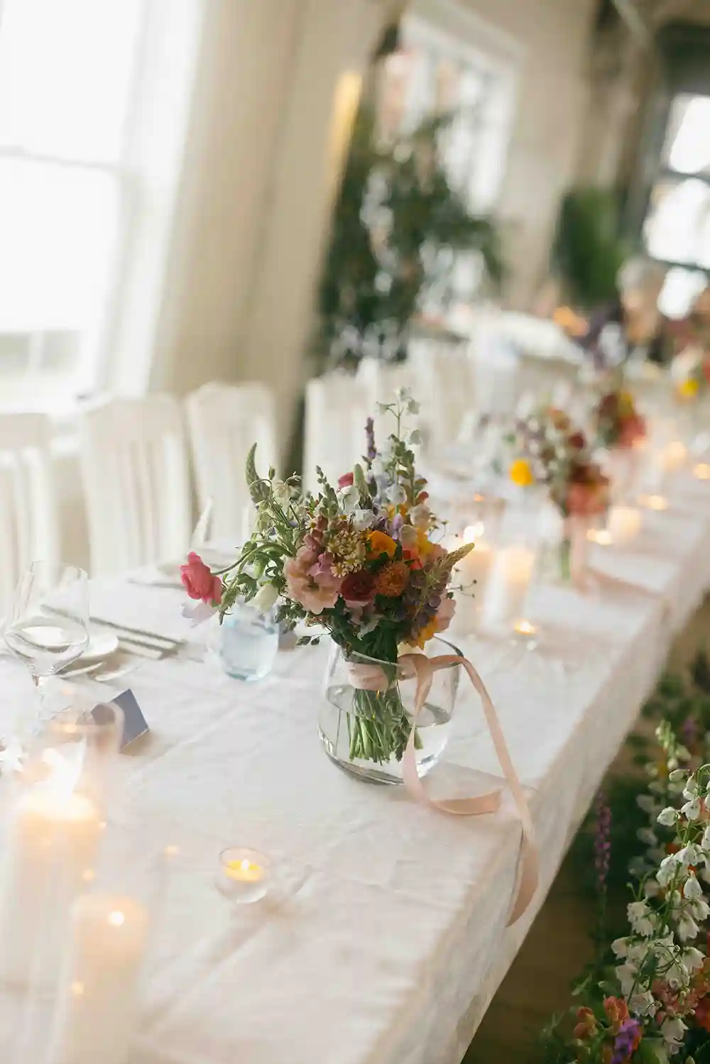 Vase on flowers on a table set for a wedding.
