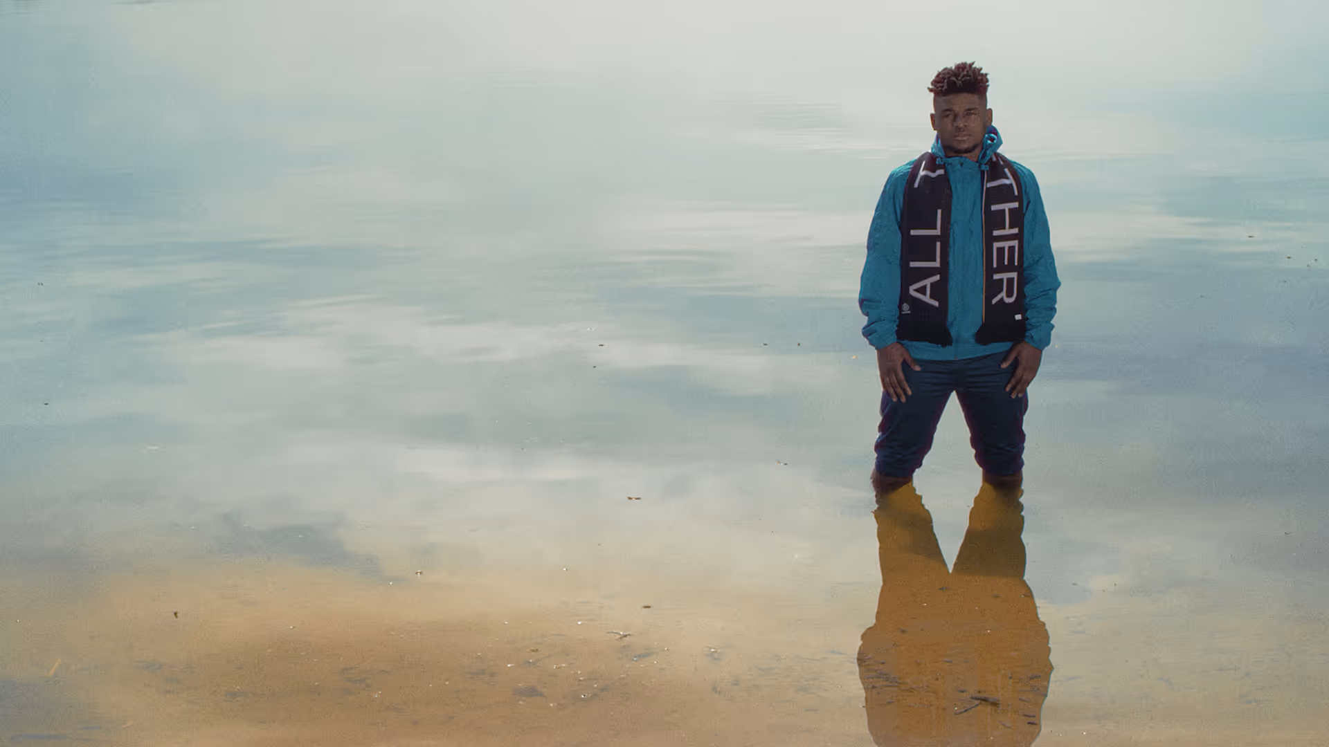 A man stands inside a lake wearing a scarf.