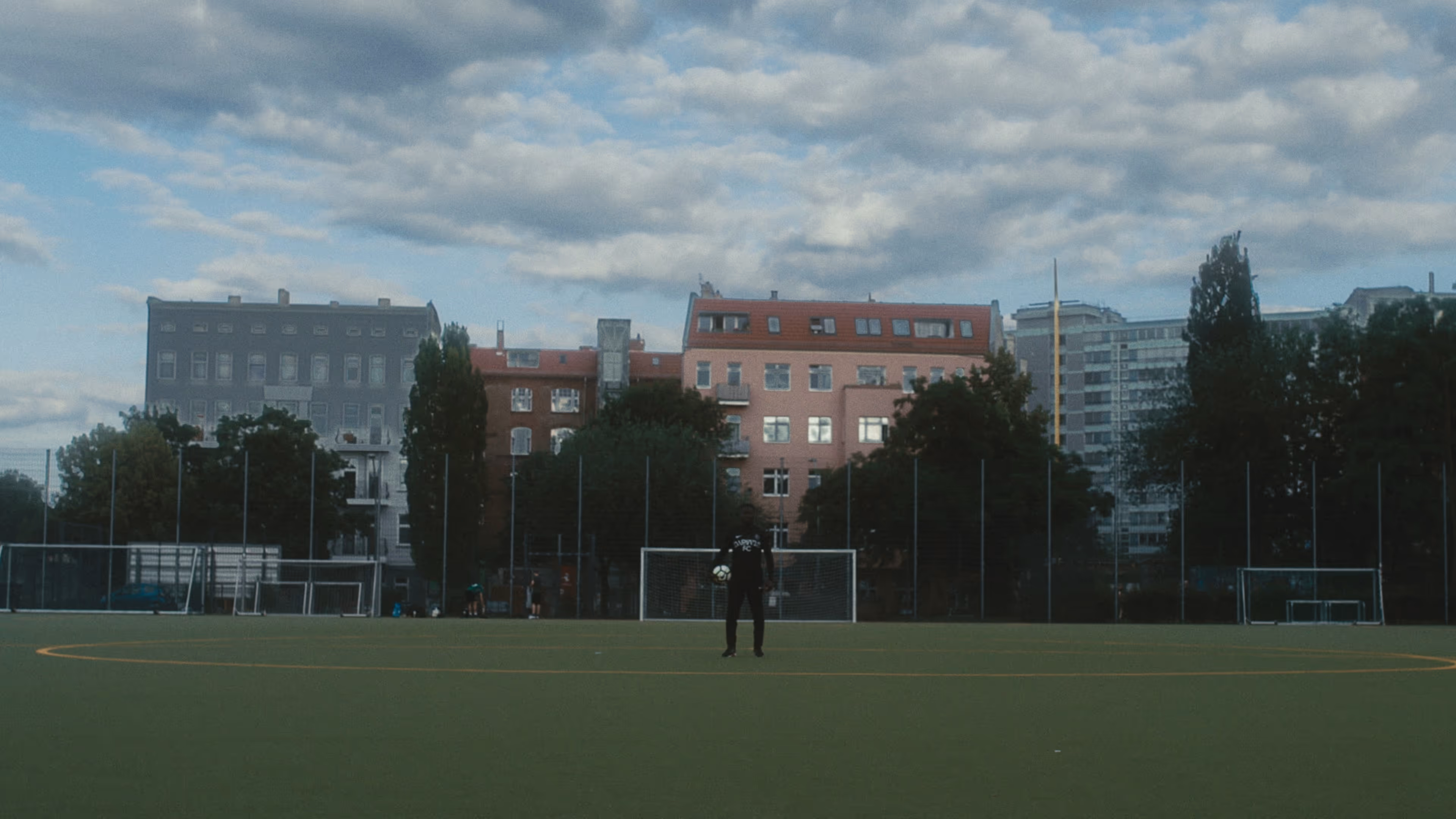 A football coach stands alone in the middle of a football pitch.