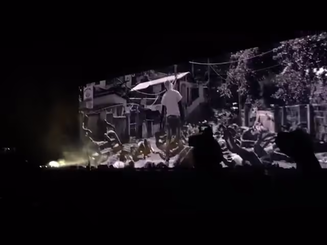 A live impression from a concert's background video where several people are on the ground and one man is still standing.