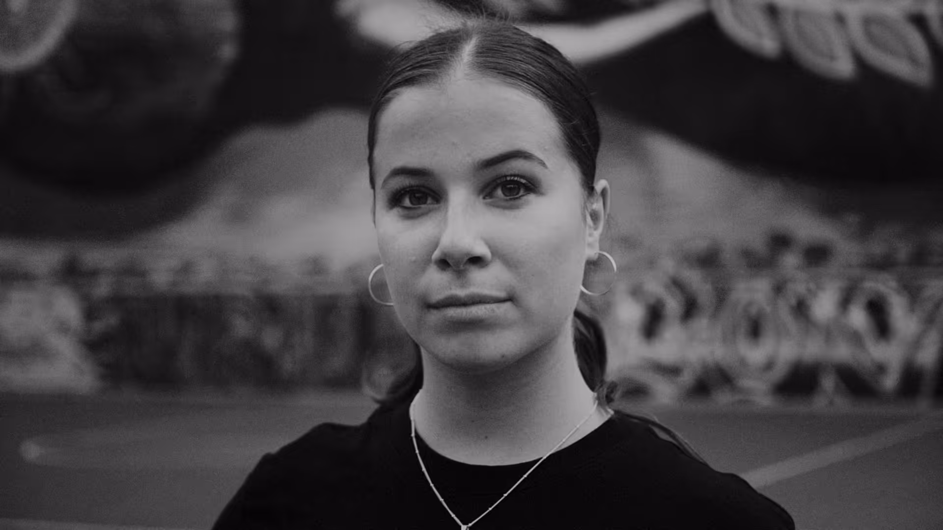 A woman faces the camera with a basketball court in the background.