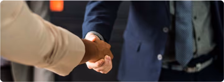 Close-up of two people shaking hands, one wearing a dark suit and blue tie, the other in a light-colored shirt.