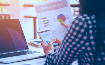 Person holding a business report with charts and graphs while using a tablet next to a laptop.