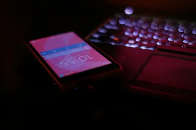Celular com tela acesa ao lado de um notebook iluminado em ambiente escuro