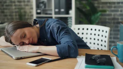 Mulher dormindo sobre o notebook em um escritório, com expressão de exaustão