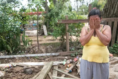 Mulher cobrindo o rosto com as mãos em situação de vulnerabilidade, com entulhos ao redor