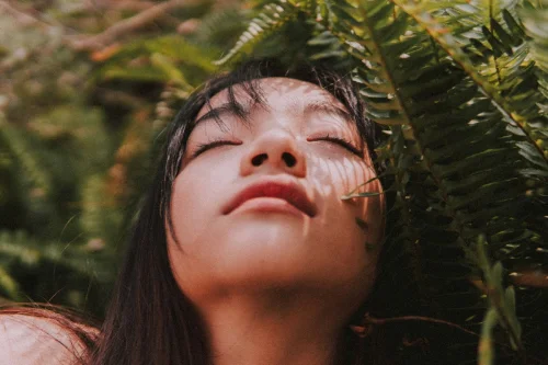 Mulher de olhos fechados relaxando em meio à natureza, simbolizando contemplação e bem-estar