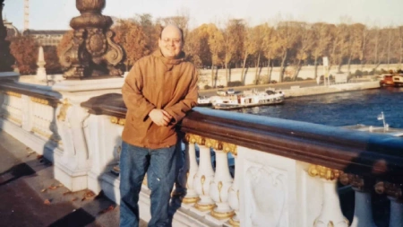 Ricardo Salztrager em Paris apoiado em ponte com rio ao fundo
