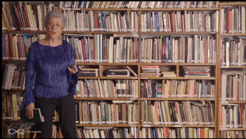 Scarlett Marton ministrando aula sobre Nietzsche diante de estante de livros