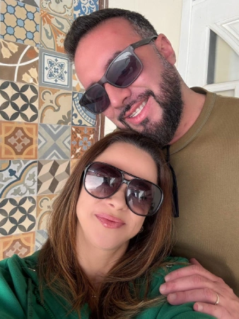 Fernanda Samico ao lado do marido Beto Zanatelli, sorrindo juntos usando óculos escuros em ambiente com azulejos decorativos