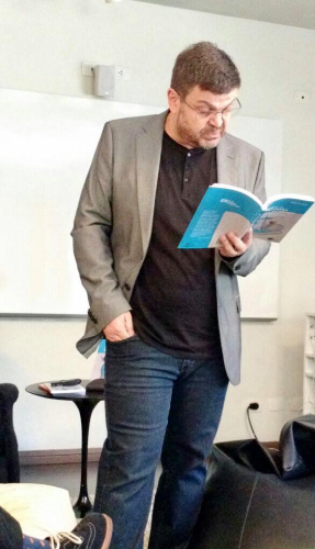 Pedro de Santi ministrando aula com livro em mãos em sala da Casa do Saber