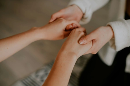 Mãos femininas segurando umas às outras em gesto de acolhimento e apoio emocional