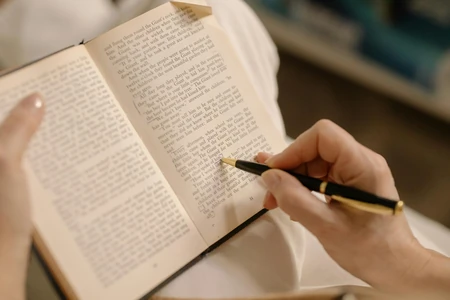Mão anotando um livro aberto com caneta.