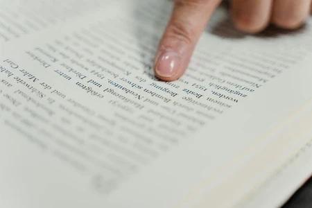 Dedos acompanhando linhas de texto em uma página aberta.