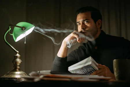 homem fumando e lendo ao lado do abajur verde