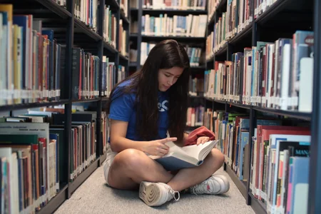 Jovem lendo livro sentada em uma biblioteca