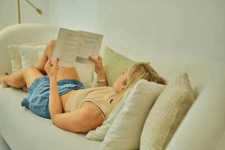 Mulher deitada no sofá lendo um livro