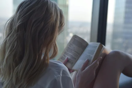 Mulher lendo um livro ao lado da janela