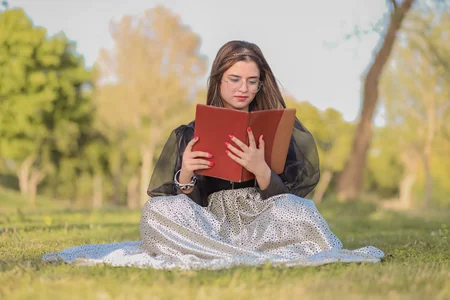Mulher sentada no gramado lendo um livro vermelho
