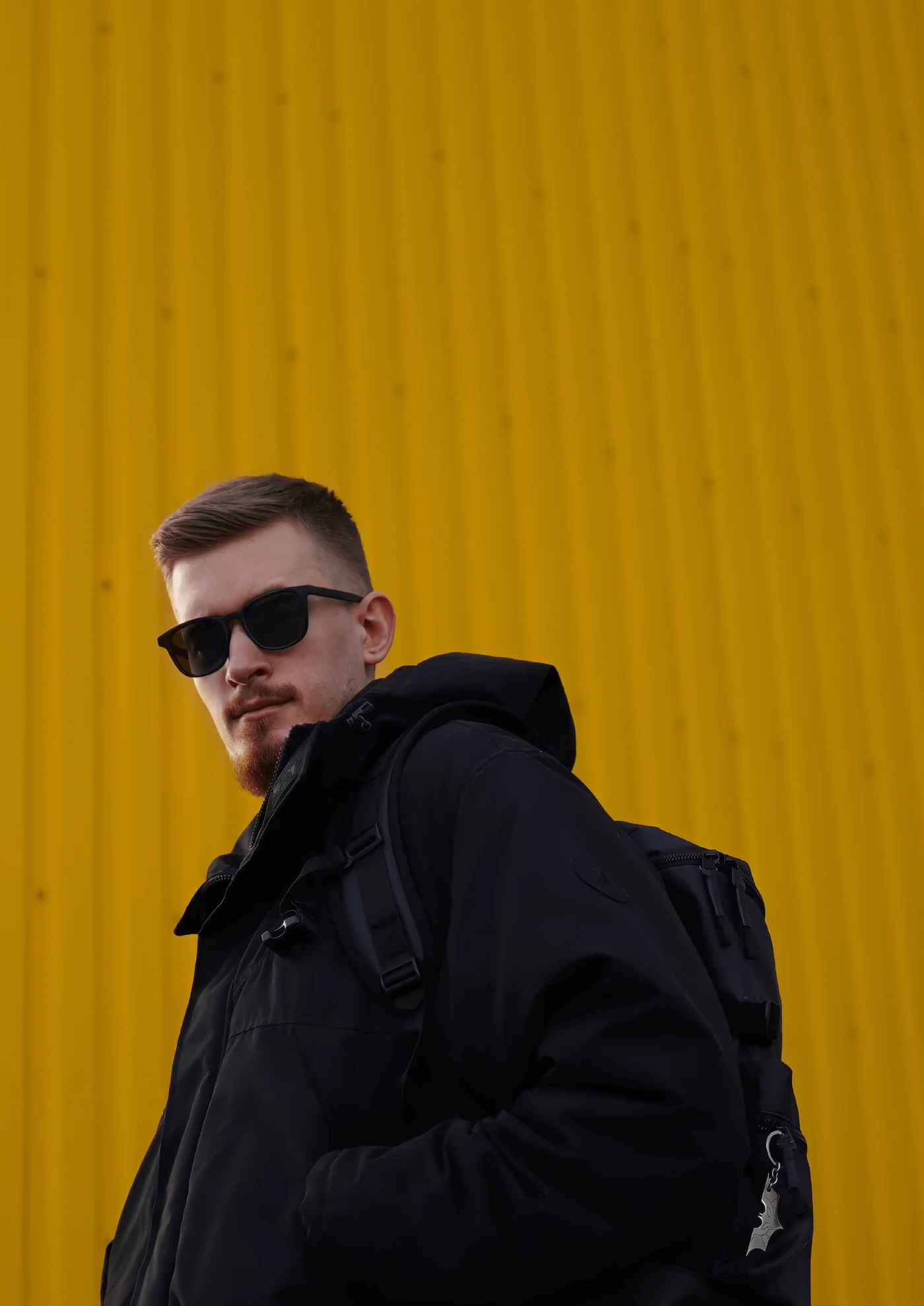 Dmitry Spravko in sunglasses and a black jacket in front of a yellow wall