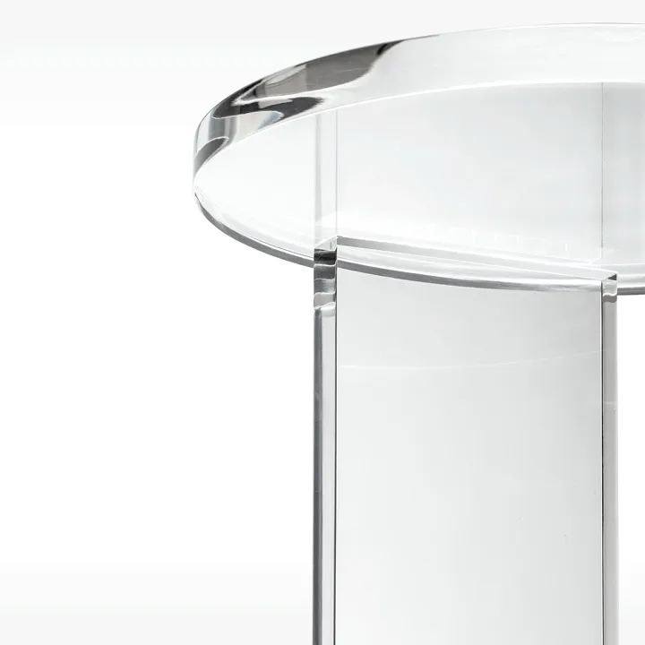 Close-up of a transparent acrylic or glass table with a round top and solid cylindrical leg.