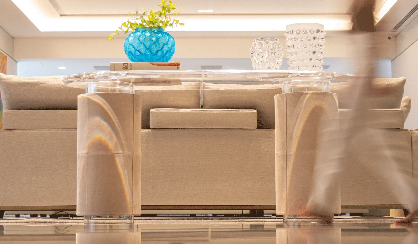 Modern beige sofa and glass table with blue vase and decorative glass items on top in living room.