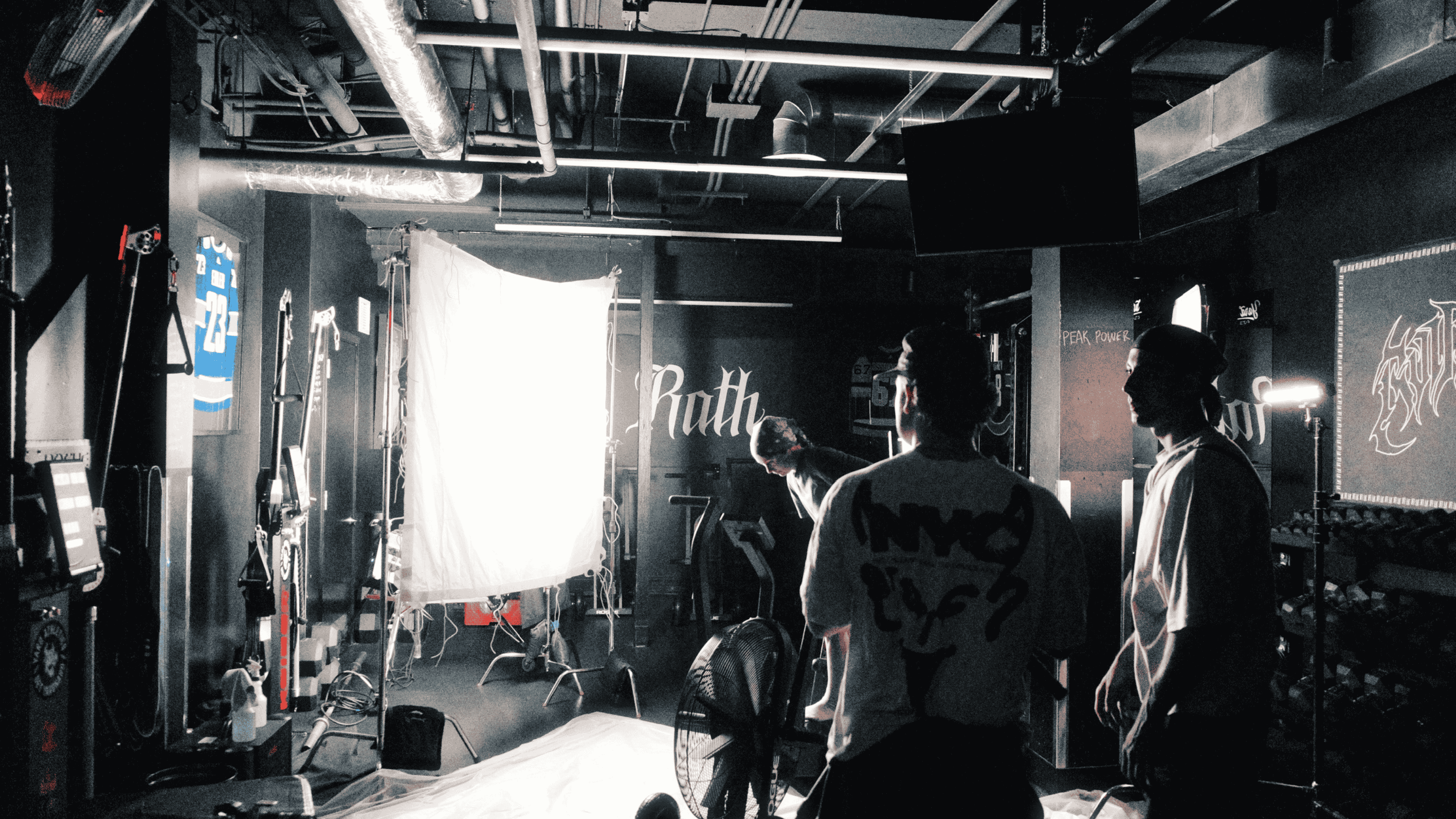 Dimly lit gym setting with three people near a large bright light panel and exercise equipment.